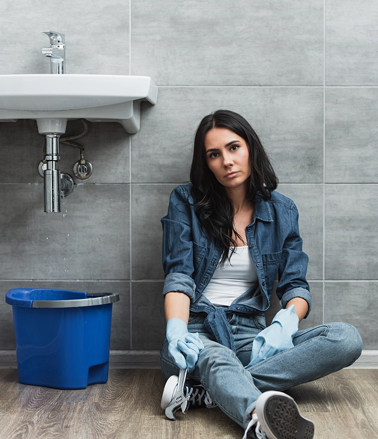 Femme assise par terre avec outillage de réparation de robinet qui fuit cherche aide